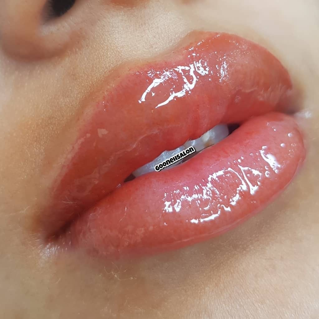 A close-up view of lips with a glossy, light pink finish, showing smooth texture and light reflection.
