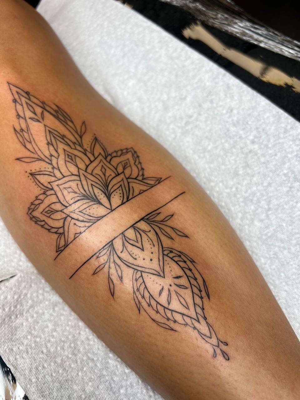 A fine-line, symmetrical mandala tattoo on a lower leg, bisected by a clean, horizontal band across the center.