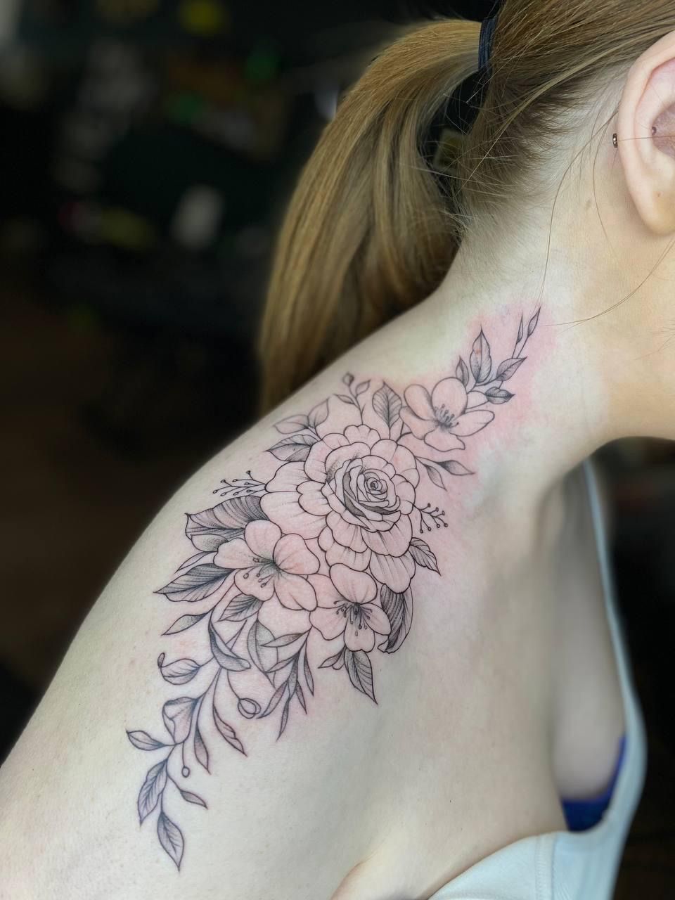 A black-ink floral tattoo featuring roses and leaves extending from the shoulder up the side of the neck.