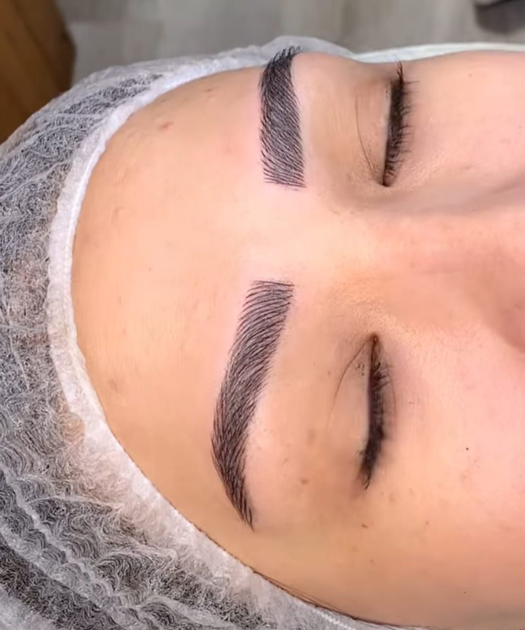A close-up of a person with freshly microbladed, hair-stroke eyebrows in a dark brown pigment.