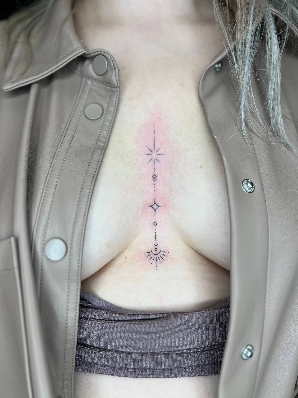 A fine-line vertical sternum tattoo featuring delicate stars and geometric elements in black ink.