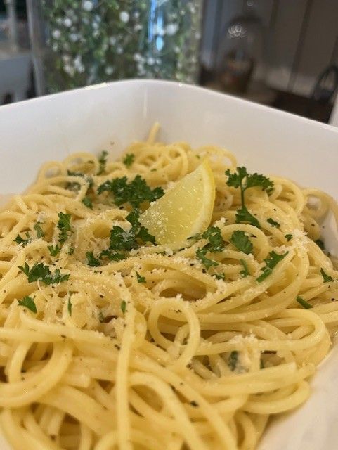Spaghetti met peterselie en geraspte kaas, gegarneerd met een schijfje citroen in een witte kom.