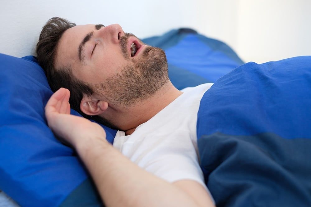 A middle aged white man is snoring in his bed and suffering with sleep apnea