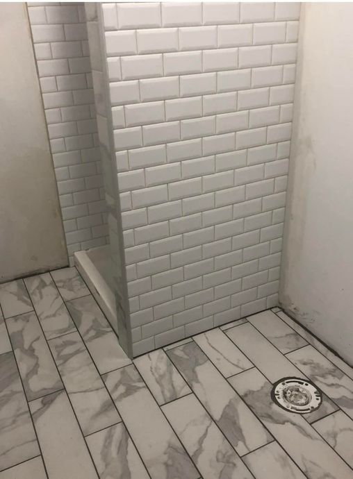 A partially tiled bathroom featuring a shower stall with white subway tiles and gray marble-look floor tiles.