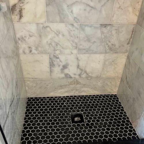 Shower stall featuring white marble wall tiles and a black hexagonal mosaic floor tile pattern with a centered drain.