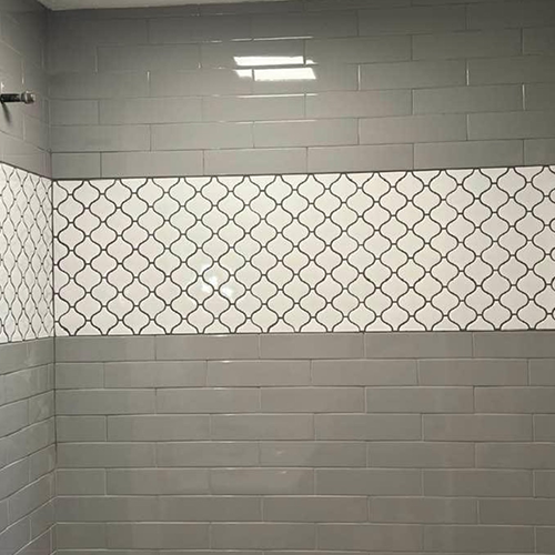A tiled bathroom wall with a section of gray horizontal subway tiles separated by a decorative white lantern-style border.