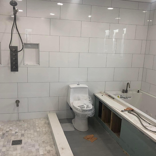 A bathroom under construction featuring white subway tile walls, a shower area, a new toilet, and a bathtub with exposed base.