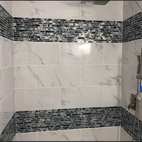 A shower interior featuring large white marble tiles accented by two horizontal rows of dark blue glass mosaic tiles.