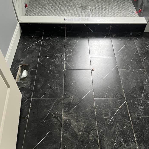 Dark marble-look floor tiles lead to a shower threshold, featuring a rectangular open floor vent on the left side.