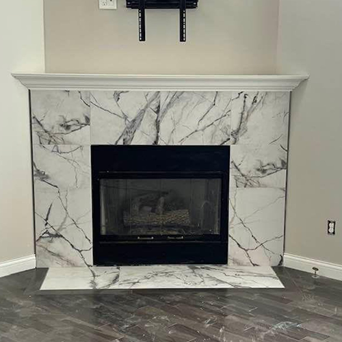 A fireplace with a white marble-look tiled surround, a black metal firebox, and a white mantel, set against gray walls.