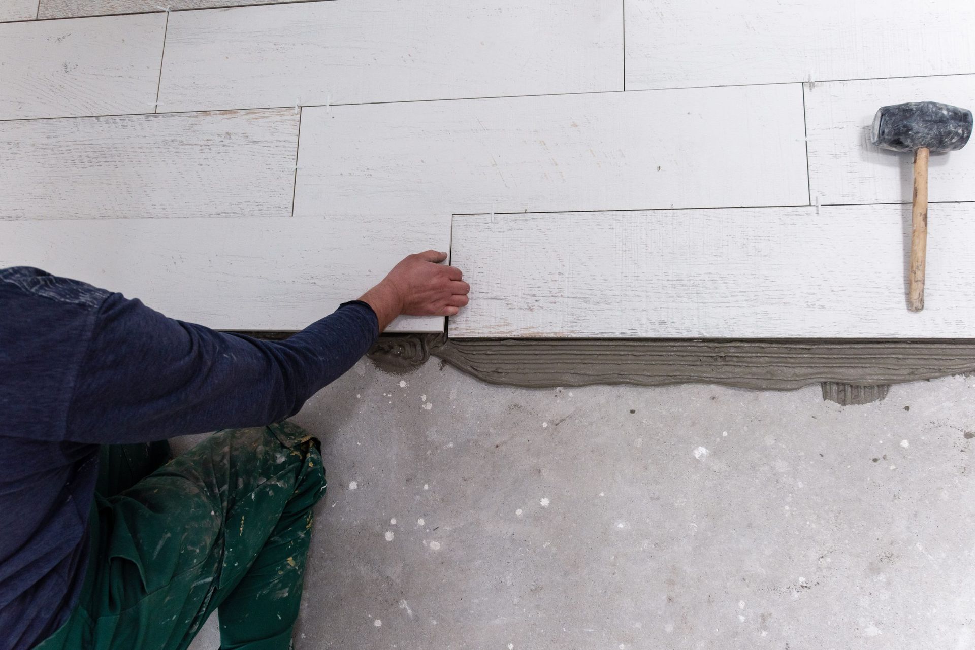 A worker in green pants places a white aerated concrete block onto a mortar-covered wall, with a mallet nearby.