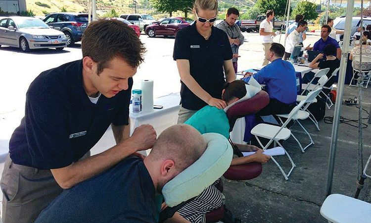 A man is giving another man a massage in a parking lot