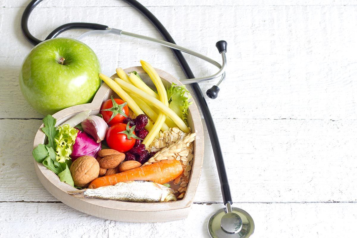 A heart shaped bowl filled with fruits and vegetables next to a stethoscope.