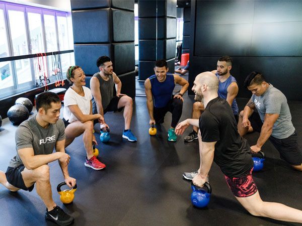 A group of people are doing exercises in a gym with kettlebells.