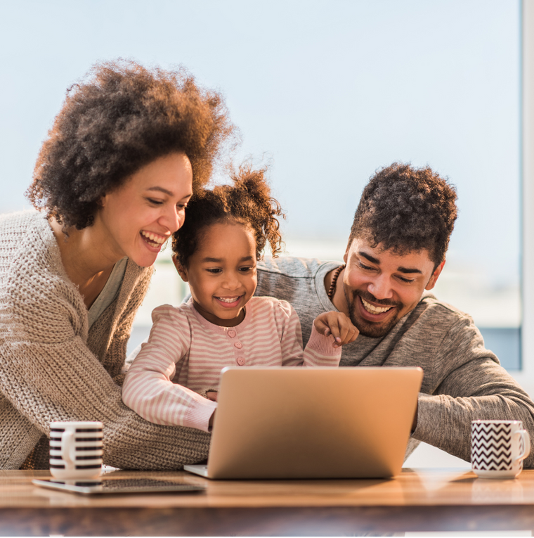 Family smiling around a laptop at a table with coffee mugs in a bright living room