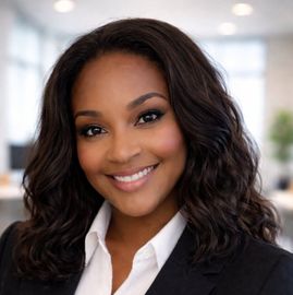 Smiling professional in a black blazer and white shirt, posing in a bright office setting