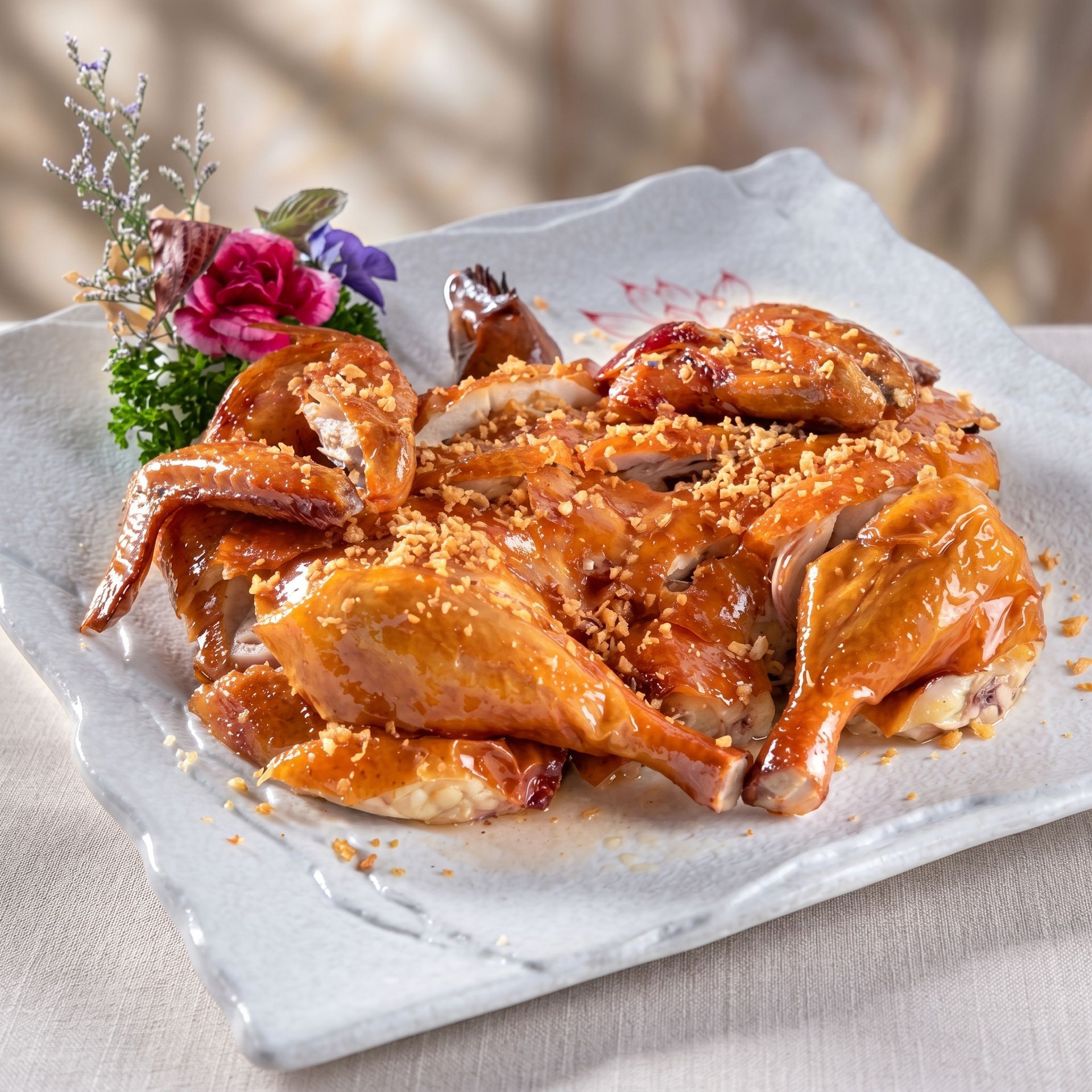 Golden roasted chicken pieces on a white platter, garnished with herbs and edible flowers.