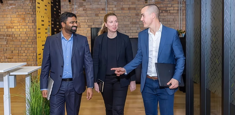 Three coworkers walking and talking in a modern office hallway