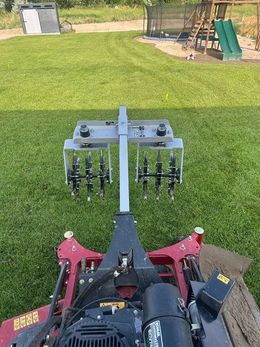 Riding lawn mower with rear aerator attachment on a green backyard lawn