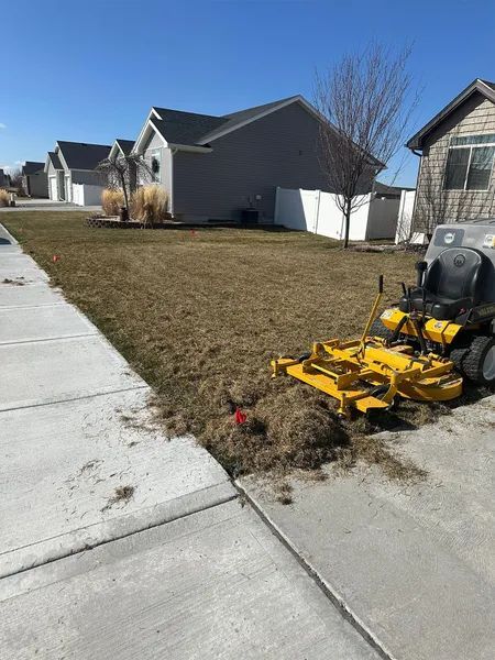 Yellow lawn mower on driveway beside a dry suburban front lawn with houses in the background
