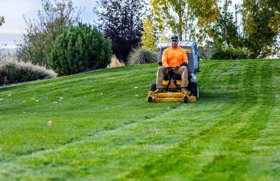 Person in orange shirt mowing a green lawn on a riding mower
