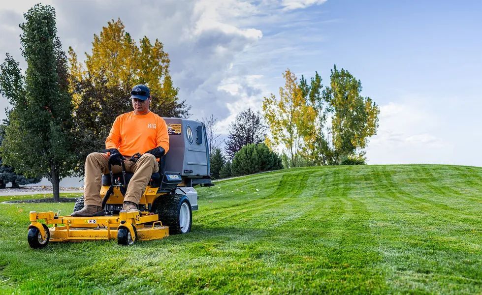 Man mowing a lush green lawn on a riding mower under a bright sky.
