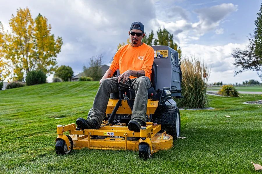 Man riding a yellow lawn mower on a grassy field under cloudy skies