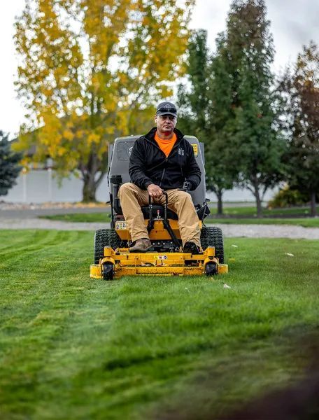 Man riding a yellow lawn mower on a green grassy field with trees in the background