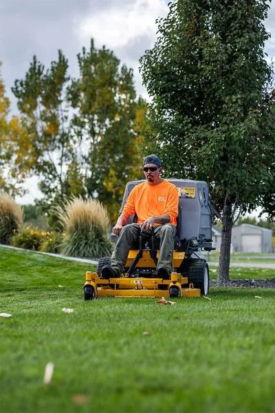 Person in an orange shirt operating a riding lawn mower on a grassy lawn