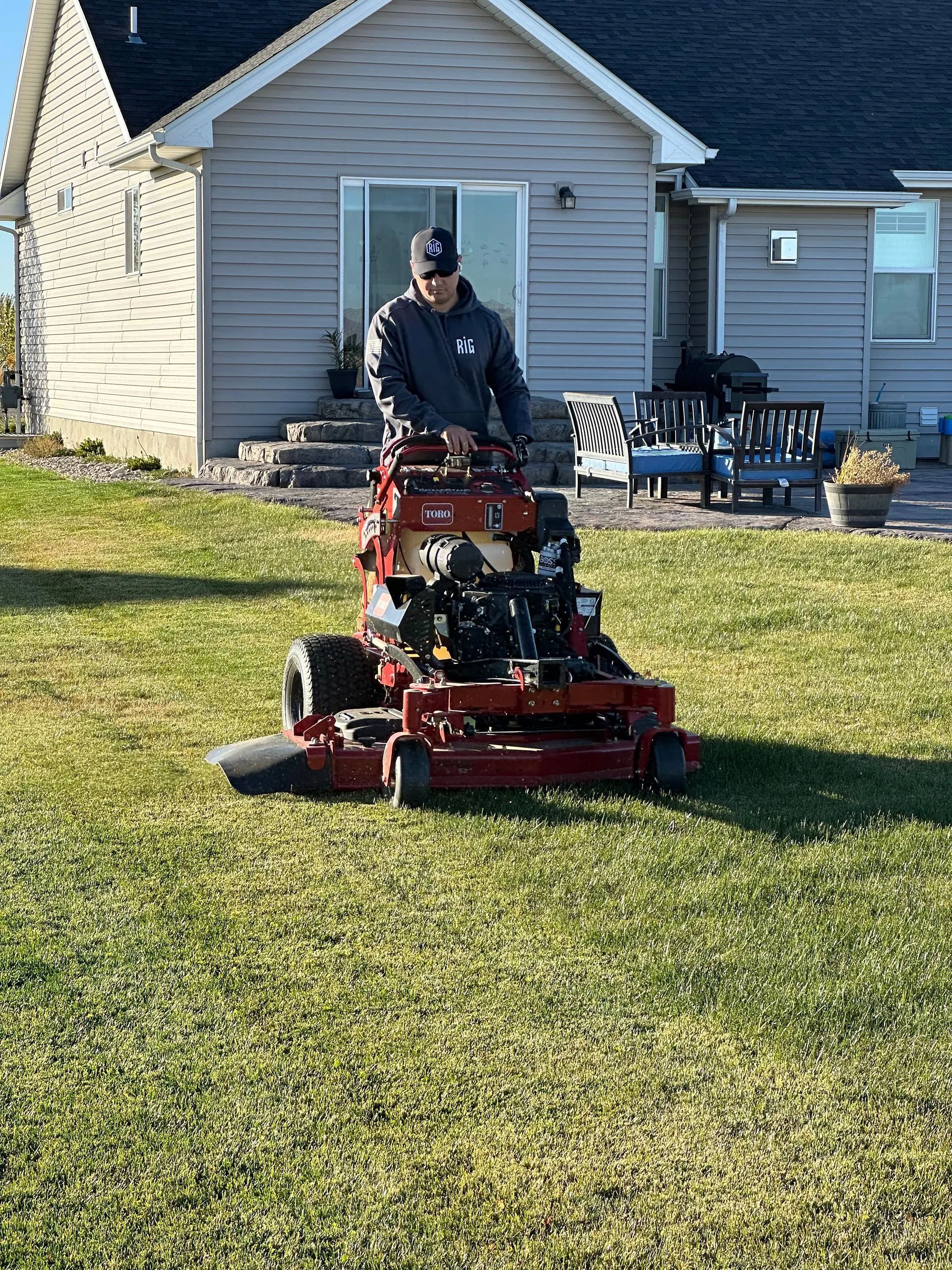 Person mowing a lawn with a red riding mower in a backyard beside a house.