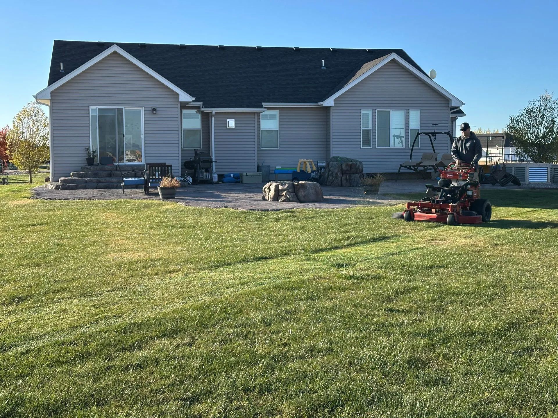 Single-story gray house with a lawn, flower beds, and several red lawn mowers in front.