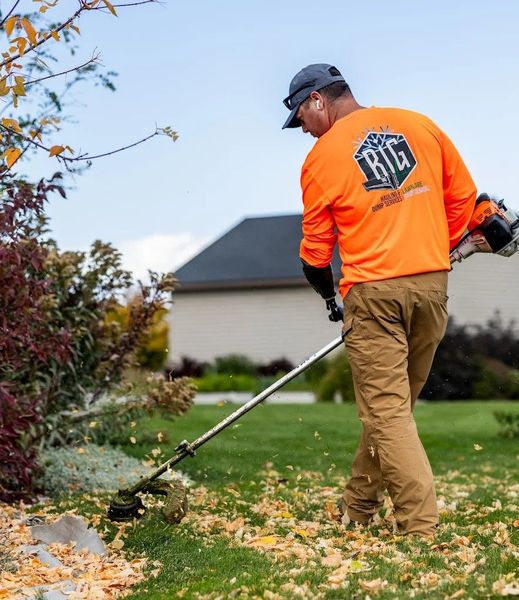 Worker in an orange shirt using a string trimmer along a grassy yard near a house.