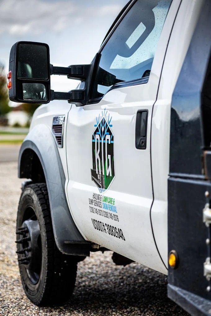 White utility truck with black trim and company logo on the door, parked on gravel outdoors
