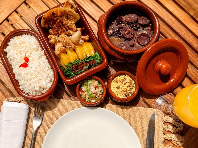 Refeição de cuscuz e tajine com pão, legumes, carne e um copo de suco de laranja sobre uma esteira trançada.