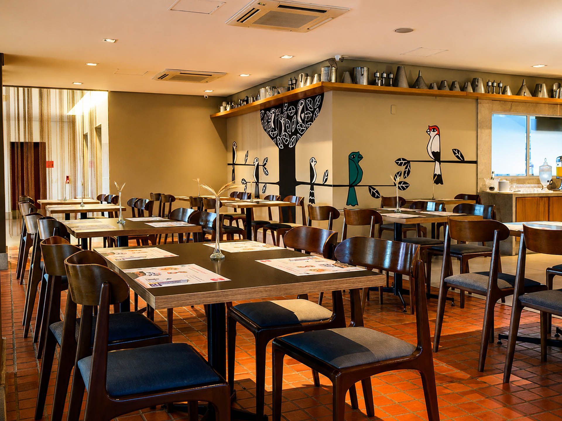 Sala de jantar vazia de um restaurante com mesas e cadeiras de madeira, iluminação aconchegante e um bar ao fundo.
