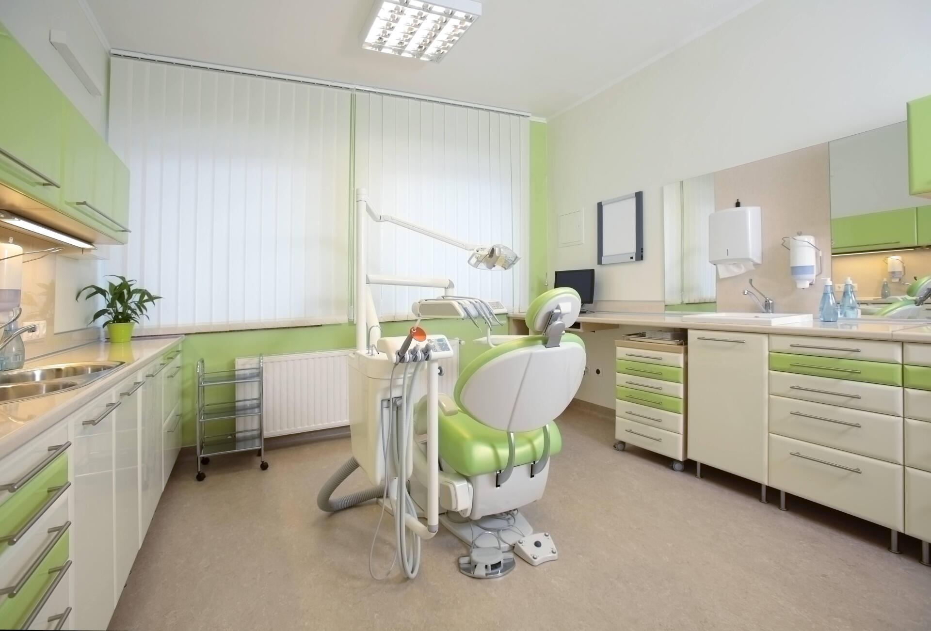 Green and white dental operatory with chair, cabinets, and equipment.