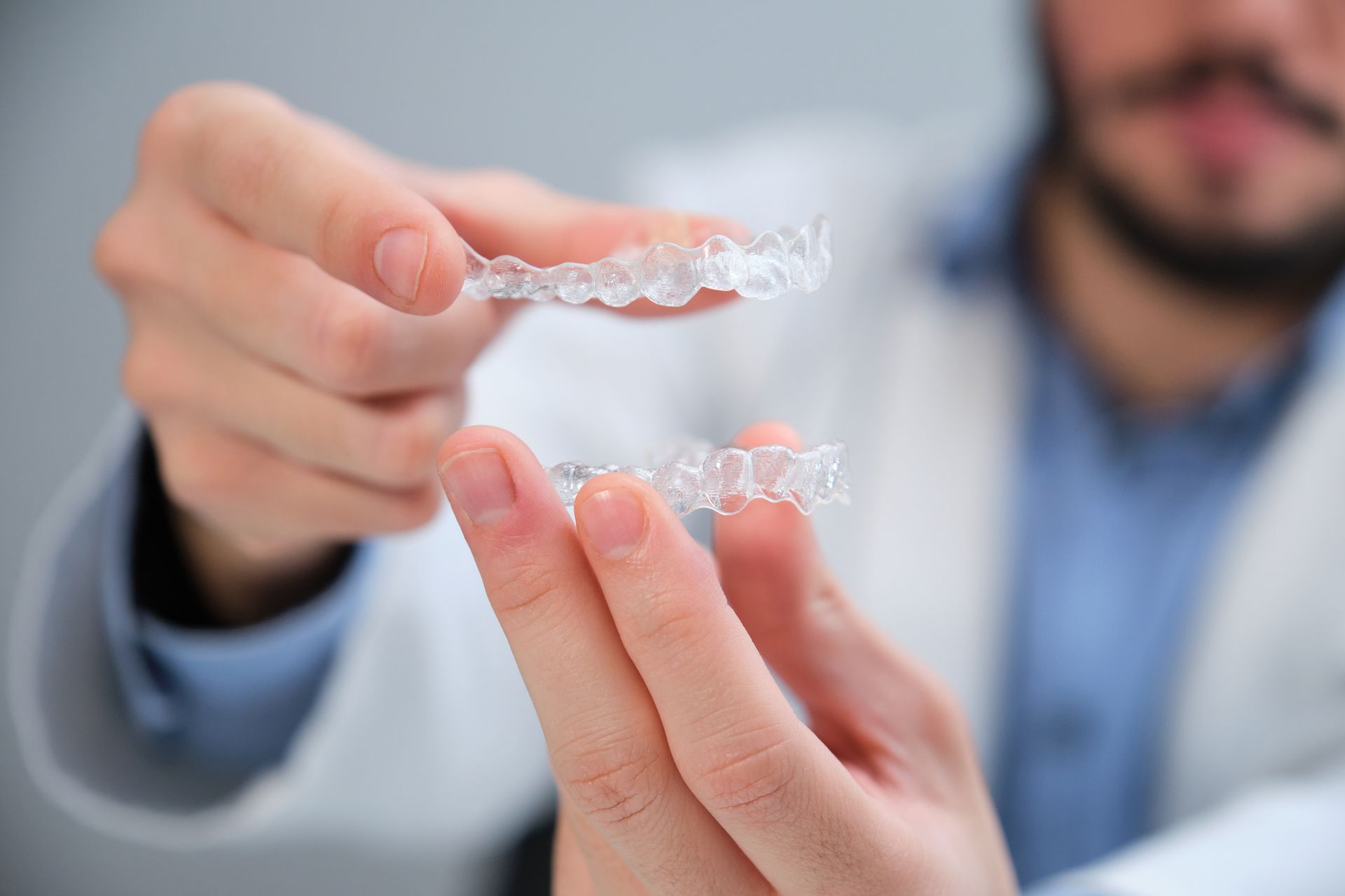 Dentist holding two clear aligners for teeth.