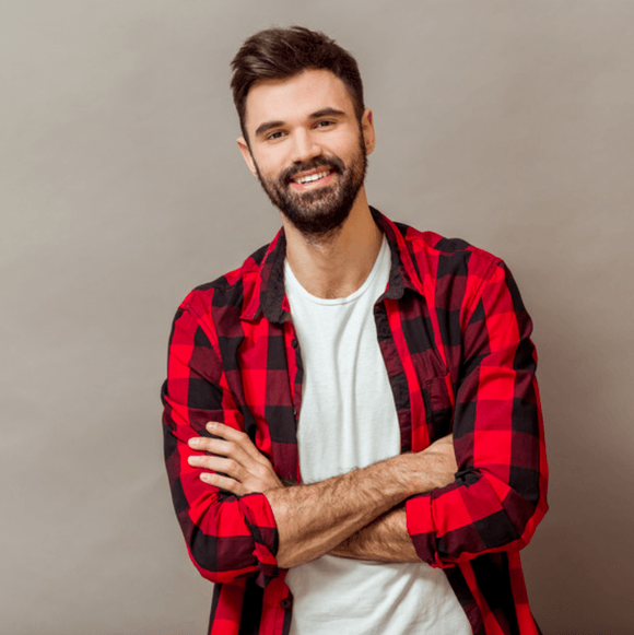 Man with beard, arms crossed, wearing a red and black plaid shirt over a white t-shirt, smiling.