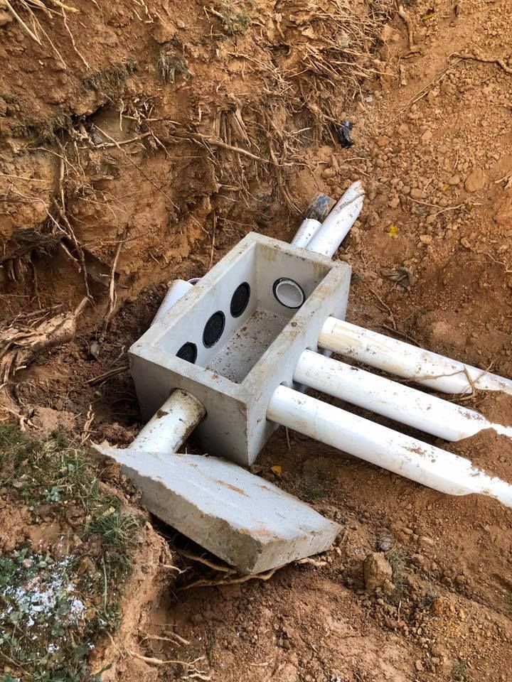 Concrete box with PVC pipes in a dirt hole. Broken concrete on the ground.
