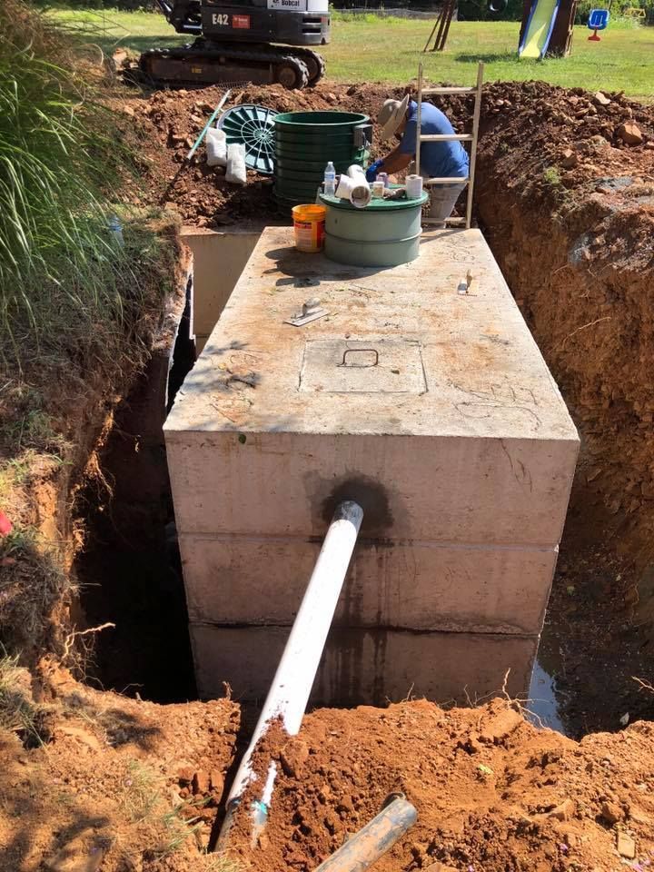 Concrete septic tank installation in a trench, worker standing on top.
