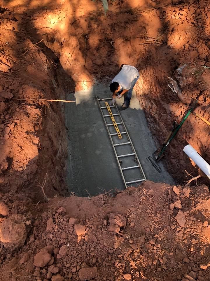 Man pouring concrete into a rectangular pit. A level sits on a ladder within.