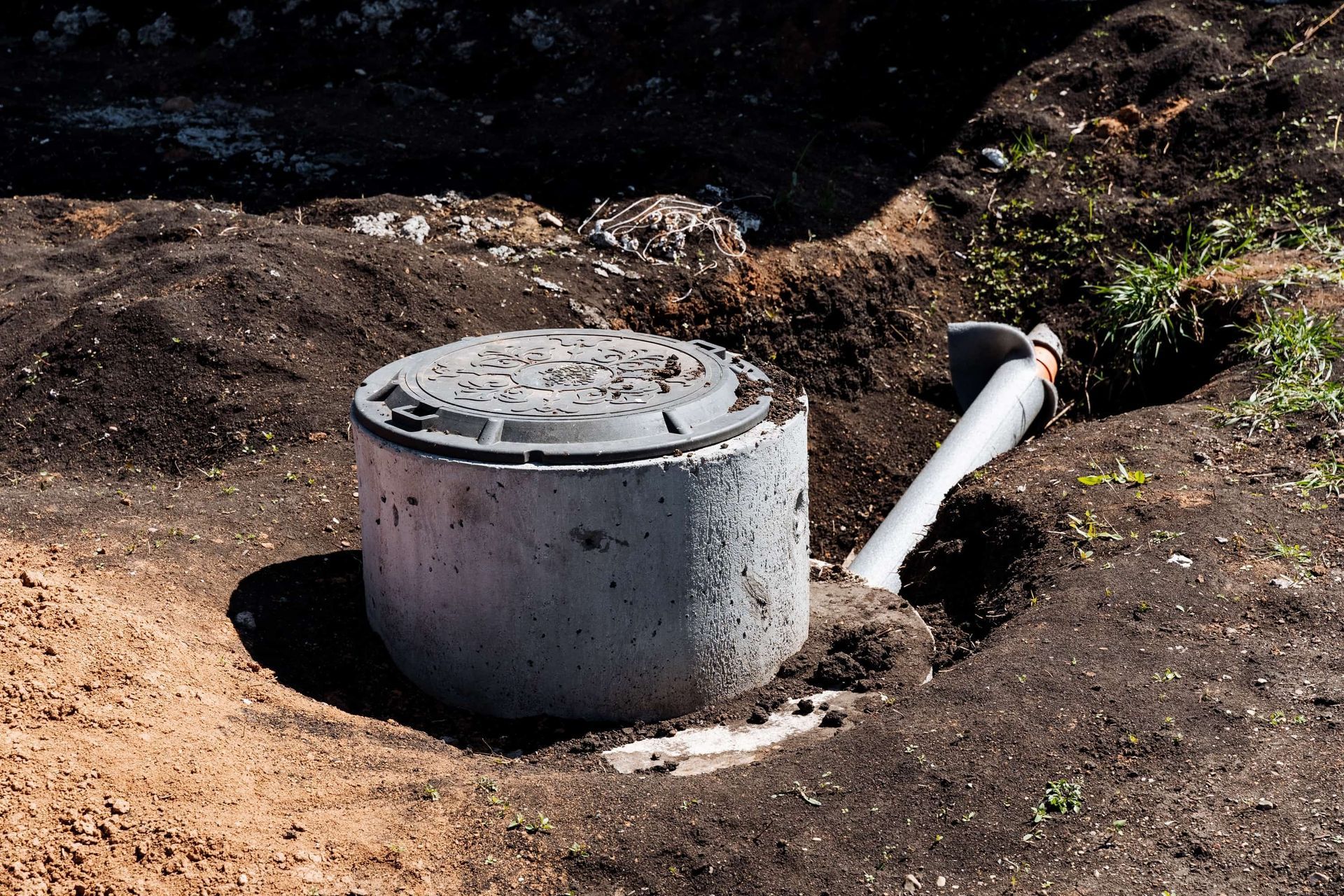 Concrete septic tank with lid, partially buried in dirt, with a white pipe.
