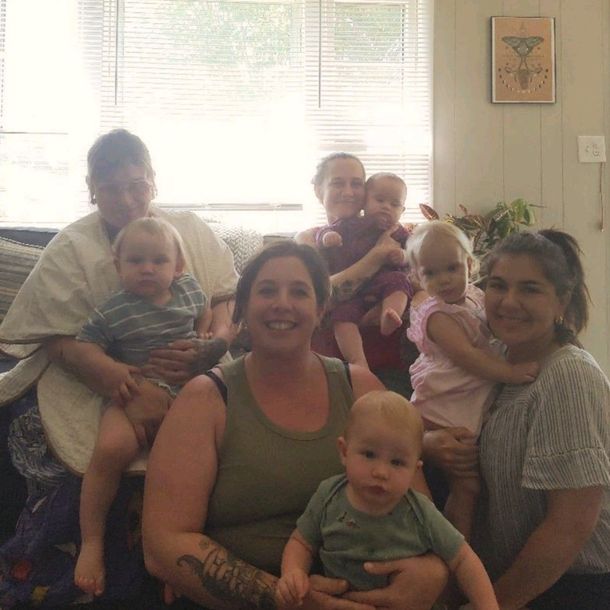 Group of people sitting together in a bright living room, smiling and holding babies.