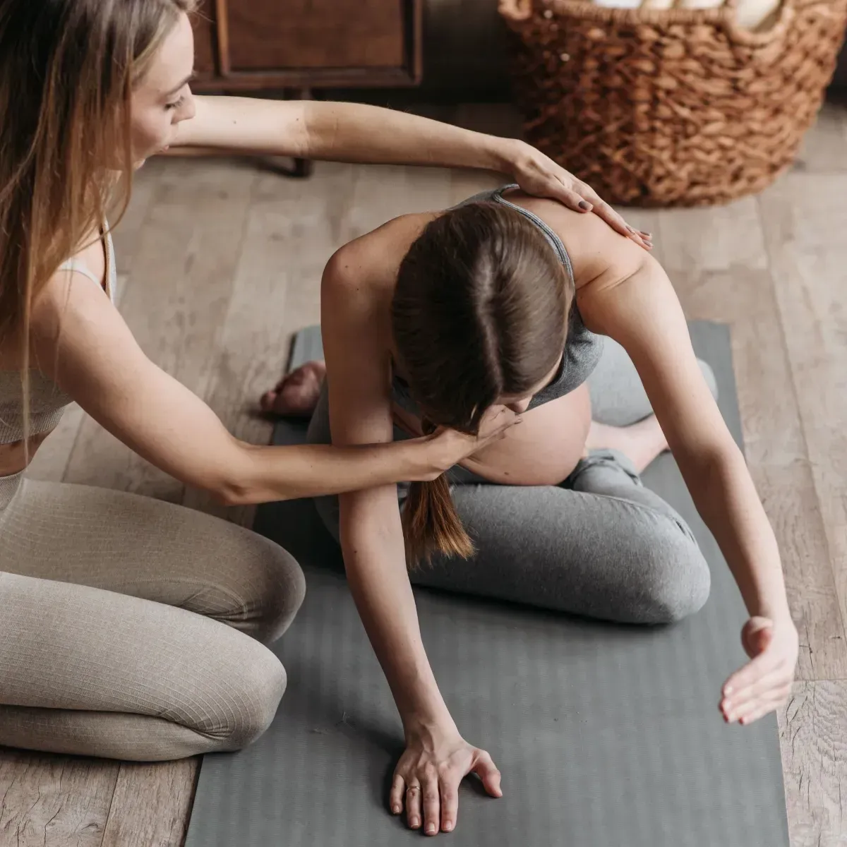 Yoga instructor gently assisting a seated person in a stretch on a mat indoors