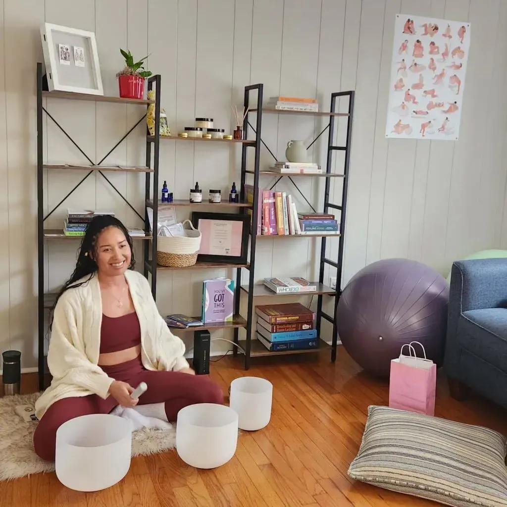 Woman sitting on a yoga mat with singing bowls in a bright living room.