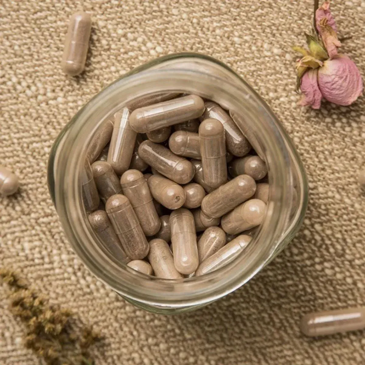 Glass jar of beige capsules on a woven mat, with dried flowers nearby