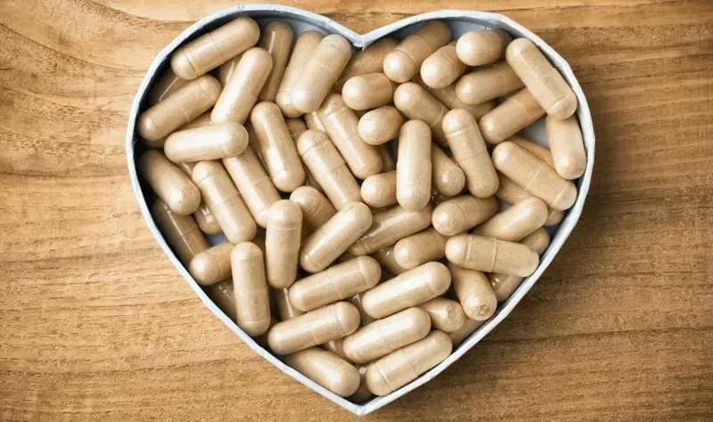 Heart-shaped bowl filled with beige capsules on a wooden surface