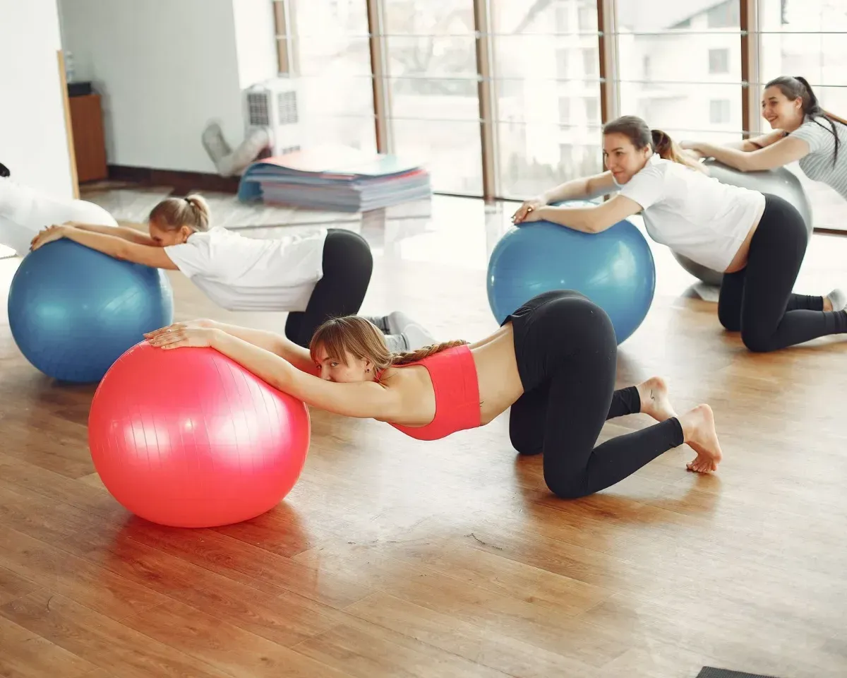 People exercising on stability balls in a bright fitness studio, stretching forward on colorful balls.