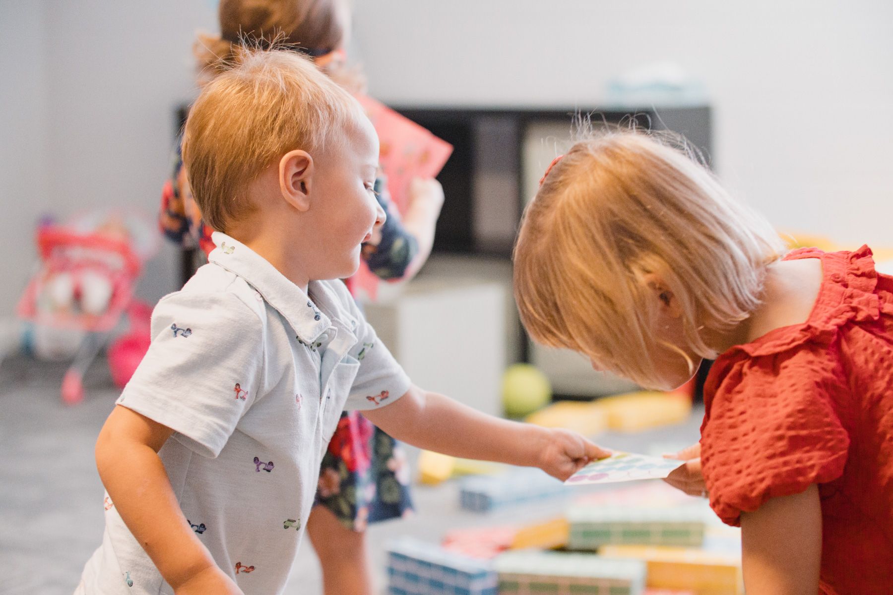 Two toddlers, one in a light blue shirt, the other in red, looking at a card together.
