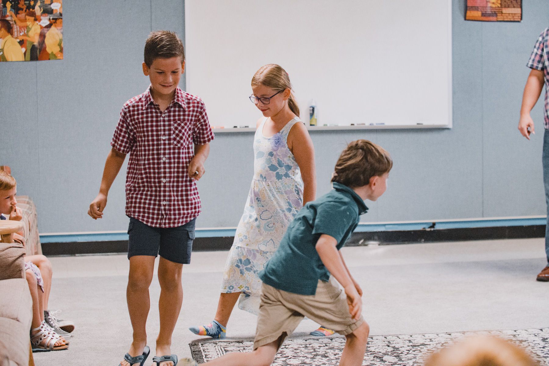 Children playing in a classroom. A boy kneels, others walk and smile.